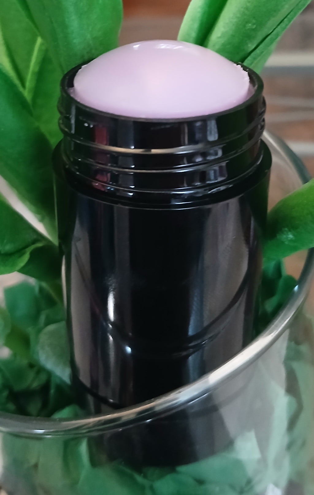 Dark Velvet Solid Perfume in a sleek black twist-up stick nestled among fresh green leaves